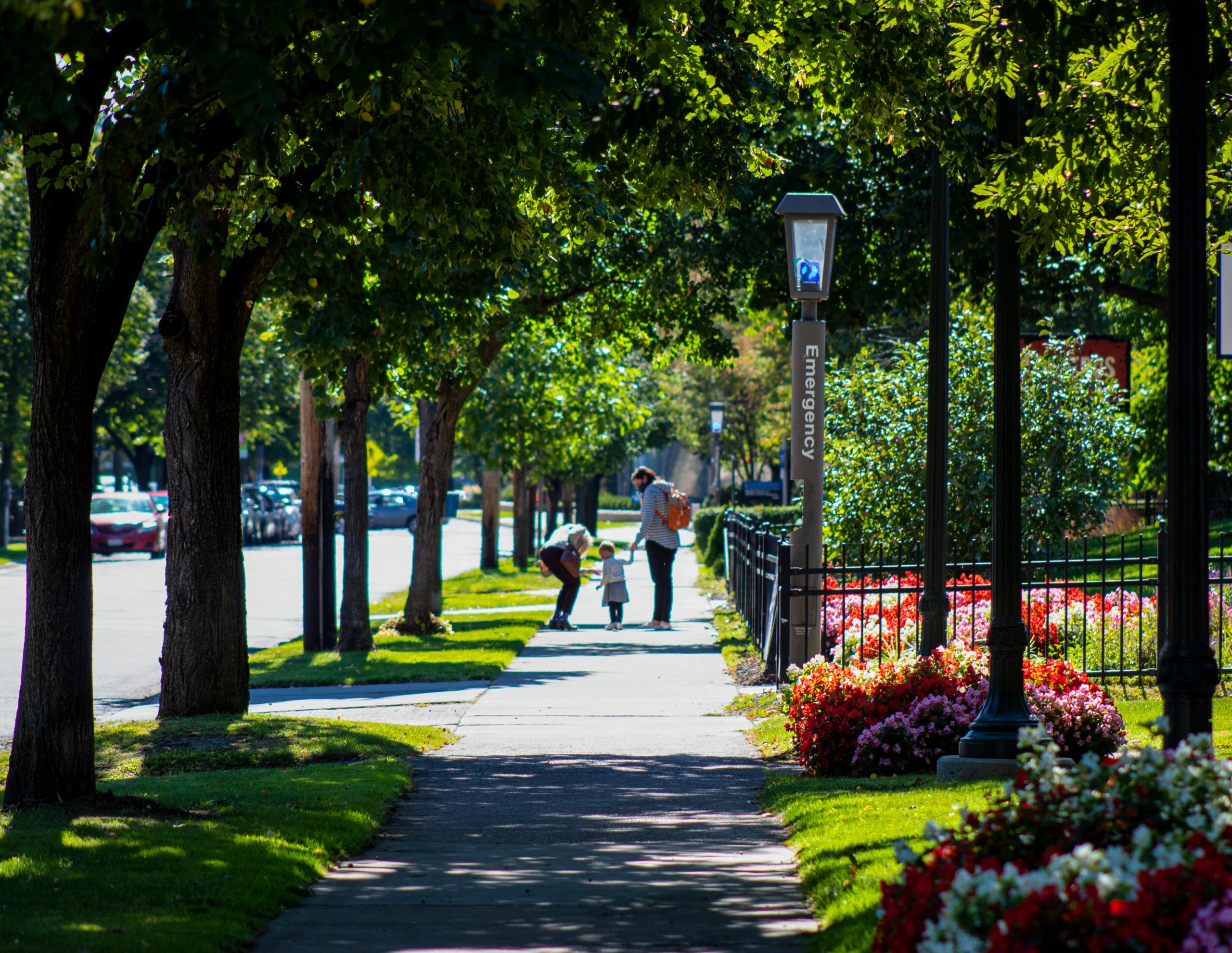 family walking down a nice sidewalk, past an emergency phone